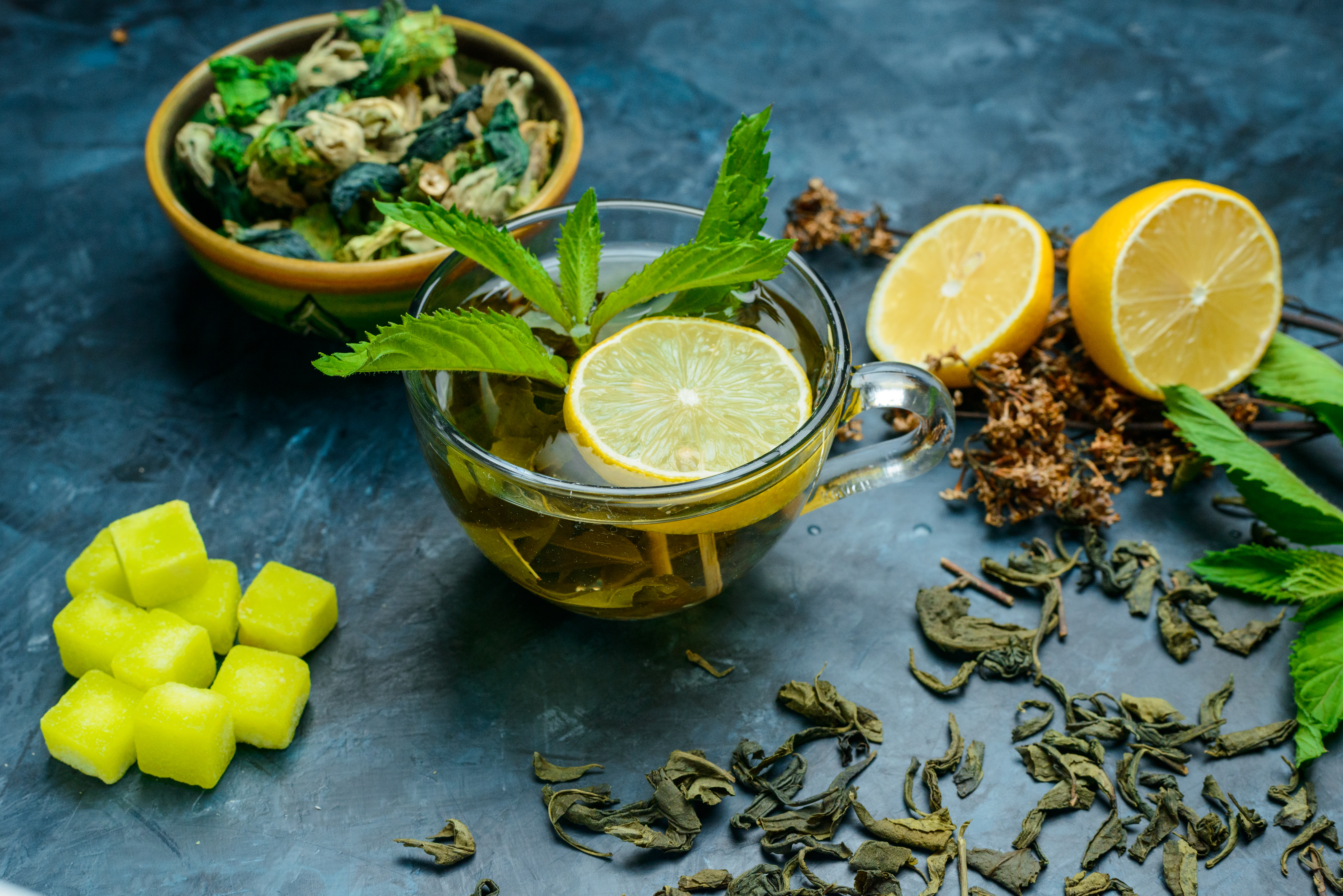 tea-cup-with-mint-dried-herbs-lemon-sugar-cubes-high-angle-view-blue-surface
